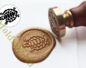 May include: A brass wax seal stamp with a wooden handle. The stamp features a turtle design. A gold wax seal with a turtle design is also shown.