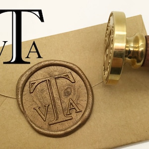 Può includere: Un timbro di cera in ottone con manico in legno, accanto a un'impronta di cera stampata su una busta marrone. Il timbro e l'impronta presentano le lettere "TVA". Il sigillo di cera è rotondo e ha un design dettagliato.