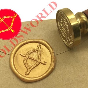Pode incluir: Um selo de cera dourado com um desenho de uma flecha e um arco. O selo está em um envelope marrom. Um carimbo dourado com uma alça de madeira está ao lado do selo.