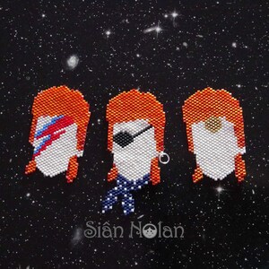 May include: Three beaded portraits of a person with orange hair, white skin, and different facial features. The portraits are against a black background with white dots.