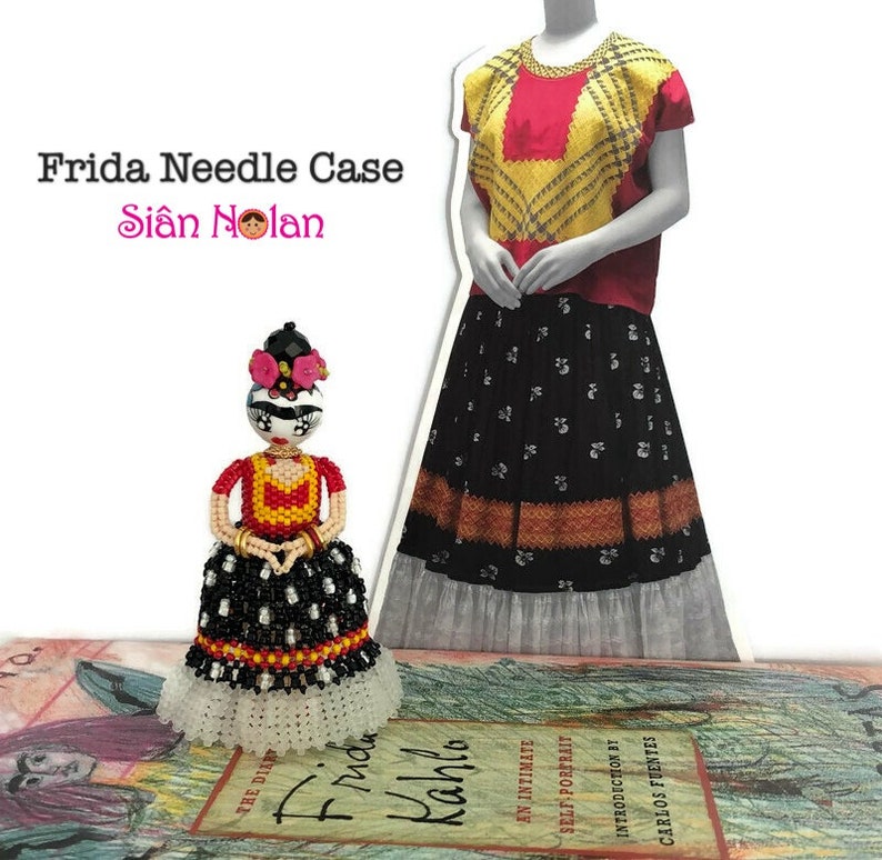 Puede incluir: Un estuche para agujas de cuentas con forma de mu&ntilde;eca Frida Kahlo. La mu&ntilde;eca lleva un vestido rojo, amarillo y negro con un borde de encaje blanco. La cara de la mu&ntilde;eca est&aacute; pintada con un dise&ntilde;o de calavera de az&uacute;car. El estuche para agujas est&aacute; sobre un libro titulado "Frida Kahlo: Un retrato &iacute;ntimo".