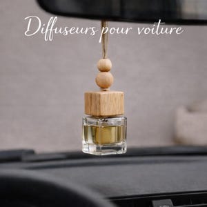 May include: A car air freshener with a wooden top and a clear glass bottle filled with a golden liquid. The freshener is suspended by a string with wooden beads. The text "Diffuseurs pour voiture" is written in cursive.
