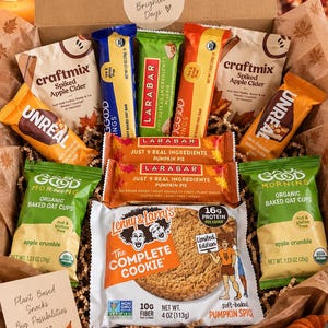May include: A cardboard gift box filled with assorted snacks including Craftmix Spiked Apple Cider packets, Larabar Pumpkin Pie bars, Unreal dark chocolate peanut butter cups, Good Morning organic apple crumble oat cups, and a Lenny & Larry's pumpkin spice cookie.