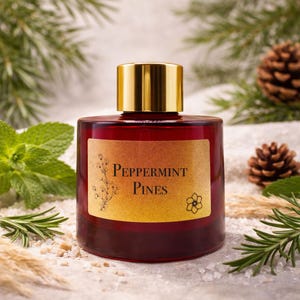 May include: A dark red glass bottle with a gold cap, labelled "Peppermint Pines." The label has a floral design and a flower. The bottle is surrounded by sprigs of mint, rosemary, pine needles, and pine cones, suggesting a natural fragrance.