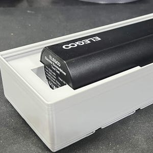 May include: A black ELEGOO Electric Screwdriver Tool Set in a white rectangular box. The screwdriver is black with white text and a yellow circle. The box has a rectangular opening to display the screwdriver.