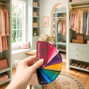 May include: A fan-shaped color palette guide labeled Dark Winter with various swatches in shades of red, pink, purple, yellow, green, and blue. The guide is held in front of a walk-in closet with light green shelving, hanging clothes, and pink boxes.
