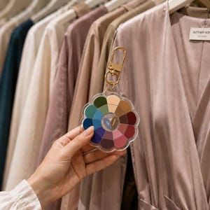 May include: A flower-shaped acrylic color palette keychain featuring twelve distinct segments in various shades including blue, green, pink, and brown, attached to a gold-toned metal lobster clasp. The center contains a small triangular label with text.