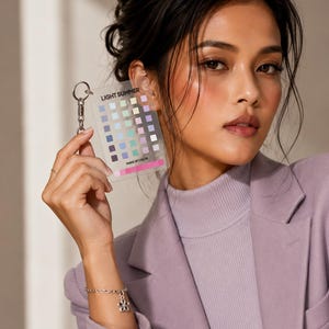 Peut inclure: Un porte-clés rectangulaire en acrylique transparent présentant une grille de petits carrés colorés, avec l'inscription LIGHT SUMMER en haut et MAKEUP COLOR en bas, fixé à un anneau et une chaîne en métal argenté, montrant des tons pastel.