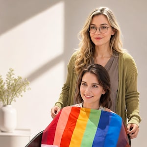 May include: A rainbow-striped salon cape featuring vertical bands of red, orange, yellow, green, blue, and purple. The fabric is smooth and lightweight, designed to drape over the shoulders and chest, with a small rectangular label on the left side.