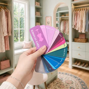 May include: A fan-shaped color palette guide labeled True Summer, featuring a spectrum of shades ranging from light pinks and purples to vibrant blues, teals, and deep grays, held open to display the individual color swatches in a sequence.