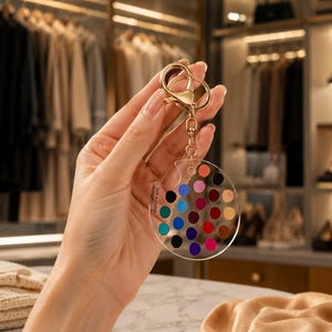 May include: A clear acrylic keyring shaped like an artist palette featuring a grid of twenty-five small, colourful circular paint swatches. The keyring includes a gold-toned metal lobster clasp and ring, with the text Soft Autumn printed on the side.