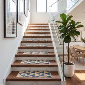 Op de afbeelding: Een set rechthoekige traptredenmatten met een geometrisch driehoekspatroon in blauw en crème. De getextureerde stoffen matten liggen op donkerhouten treden met witte marmeren stootborden in een trap met een glazen leuning.