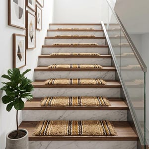 Puede incluir: Un conjunto de alfombrillas rectangulares para escaleras con pelo largo y texturizado en tonos beige, amarillo mostaza y marrón oscuro con patrones de rayas verticales, instaladas sobre peldaños de madera con contrahuellas de mármol blanco.