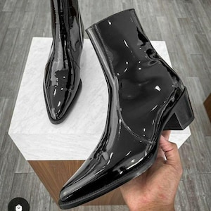 May include: Black patent leather ankle boots with a pointed toe and a block heel. The boots have a glossy finish and a side zip. The heel height is approximately 5 cm.