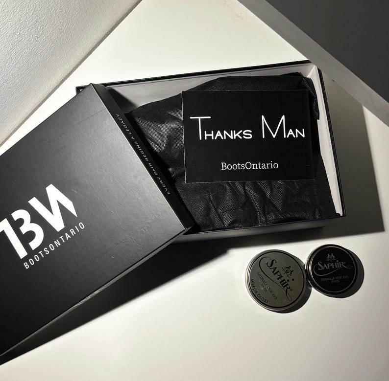 May include: Black box with the text "13W BOOTSONTARIO" and "EVERY PAIR BEGINS A LEGACY". Inside the box is black tissue paper and a card saying "Thanks Man BootsOntario". Two silver shoe polish tins are also visible.
