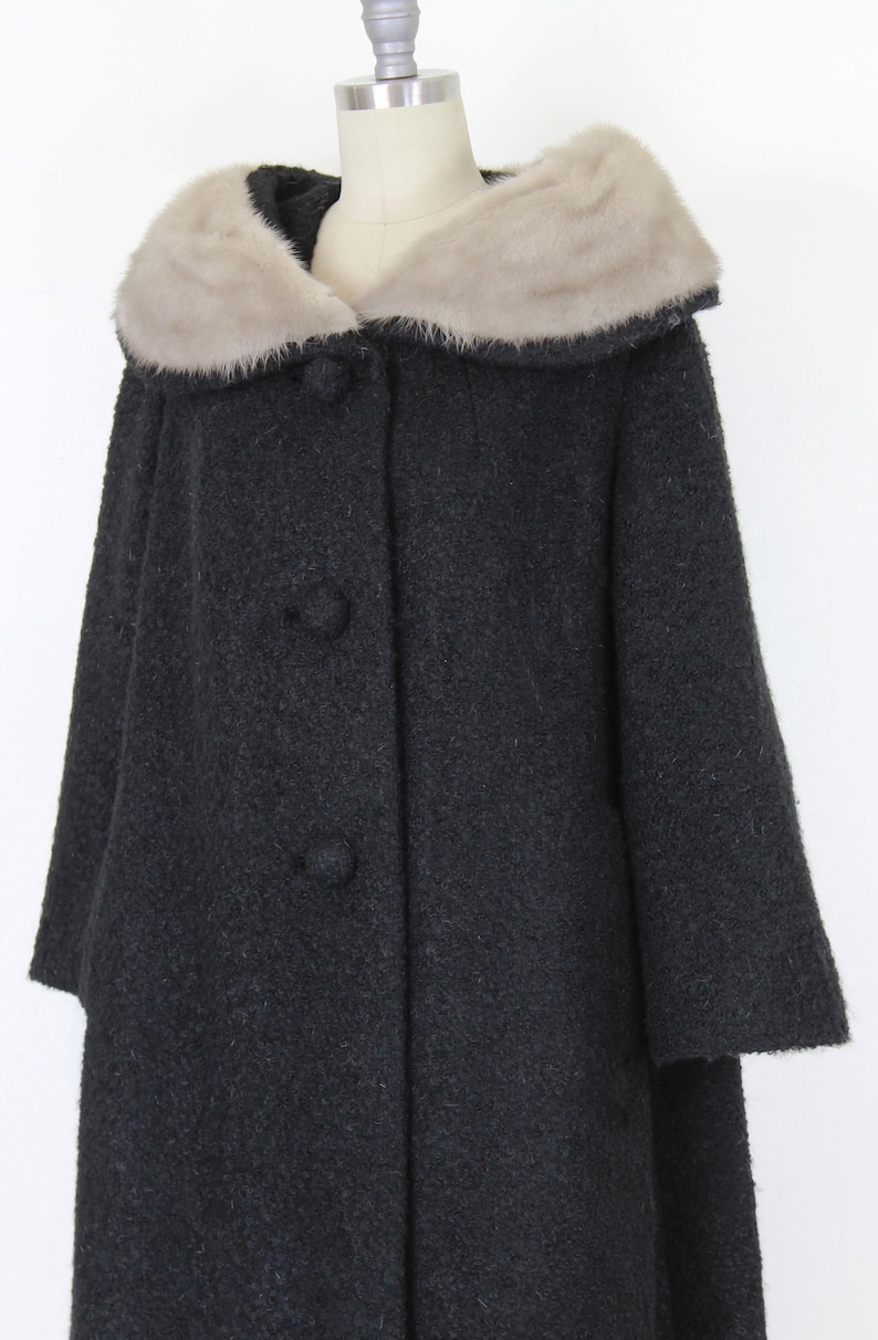 Puede incluir: Un abrigo negro vintage con cuello de piel sint&eacute;tica. El abrigo tiene una botonadura frontal y una silueta acampanada. El cuello es de color beige claro, contrastando con el abrigo oscuro. El abrigo se exhibe en un maniqu&iacute;.
