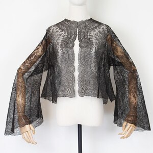 May include: A black lace jacket with wide, bell sleeves. The jacket is displayed on a mannequin against a white background. The intricate floral lace pattern is visible throughout the garment, creating a delicate and elegant look.