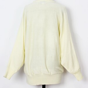 May include: A pale yellow knitted sweater with long sleeves and a ribbed hem.