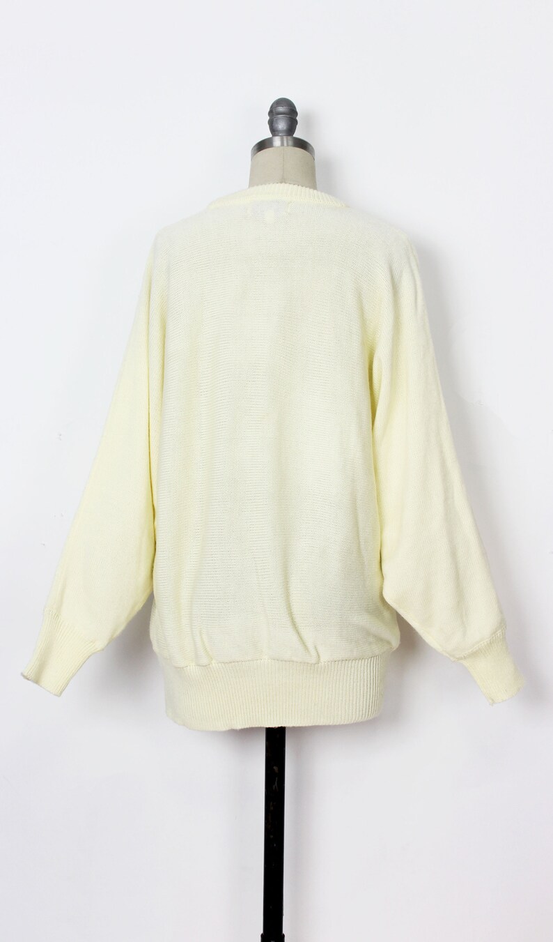 May include: A pale yellow knitted sweater with long sleeves and a ribbed hem.
