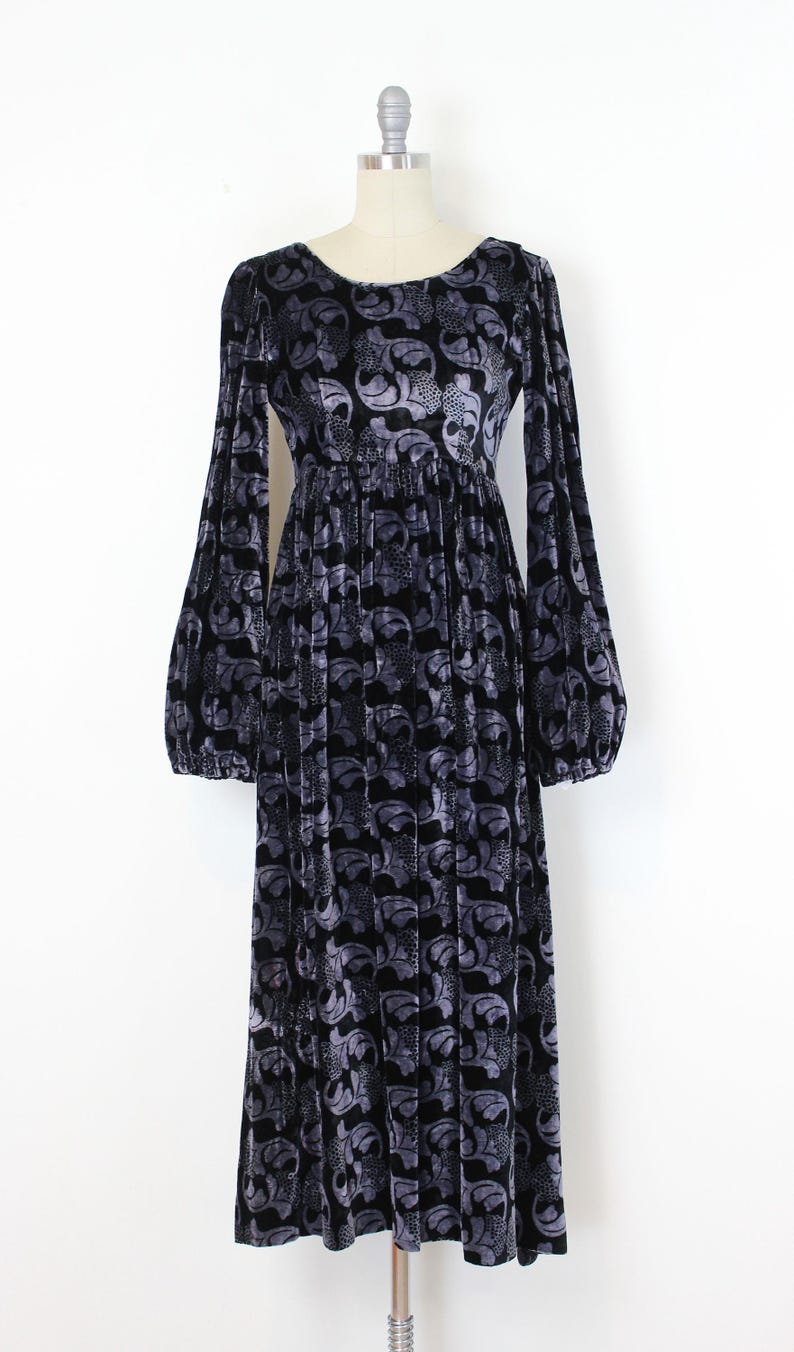 May include: Black velvet dress with a gray floral pattern. The long-sleeved dress has a round neckline and a gathered waist. The dress is displayed on a mannequin.