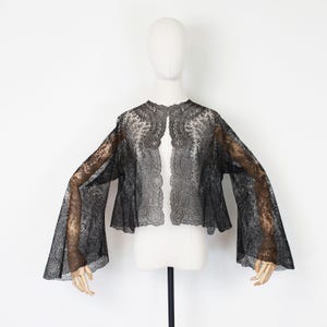 May include: A black lace jacket with wide, flared sleeves. The open-front jacket is displayed on a mannequin against a white background. The intricate lace design is visible throughout the garment, creating a delicate and elegant look.
