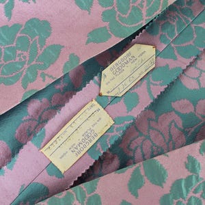 May include: Close-up of a pink and teal floral fabric with the text "BERGDORF GOODMAN NEW YORK" on two attached tags. The fabric features a repeating pattern of stylized roses.