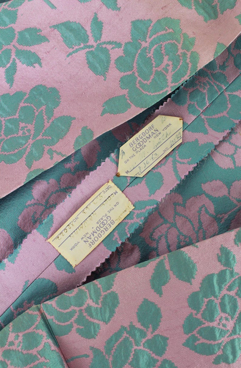 May include: Close-up of a pink and teal floral fabric with the text "BERGDORF GOODMAN NEW YORK" on two attached tags. The fabric features a repeating pattern of stylized roses.