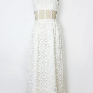 May include: White sleeveless maxi dress with a high neckline and floral eyelet pattern. The dress features a sheer panel at the waist. The dress is displayed on a mannequin.