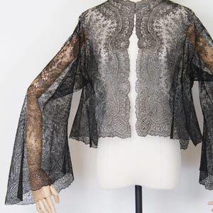 May include: Black lace bolero jacket with wide, flared sleeves. The open-front jacket features intricate floral and paisley patterns throughout the delicate fabric. The garment is displayed on a mannequin against a white background.