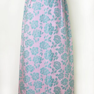 May include: A vintage-style dress with a pink background and a repeating pattern of teal roses. The dress has a fitted bodice and a flared skirt, ideal for a formal event or special occasion. The fabric has a subtle sheen.