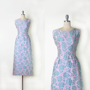 May include: A vintage, sleeveless dress in a light pink hue, adorned with a repeating pattern of teal-colored floral designs. The dress features a fitted bodice, a defined waist, and a flowing skirt, displayed on a dress form.