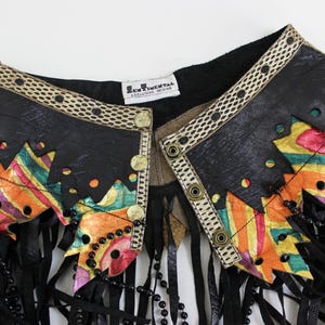 May include: A black leather jacket collar with colorful geometric accents and fringe. The collar features a decorative trim, gold buttons, and a beaded necklace. The label reads "SENTIMENTAL EXCLUSIVE DESIGN."