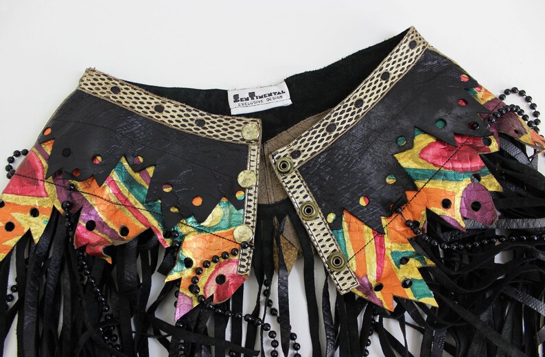 May include: A black leather jacket collar with colorful geometric accents and fringe. The collar features a decorative trim, gold buttons, and a beaded necklace. The label reads "SENTIMENTAL EXCLUSIVE DESIGN."