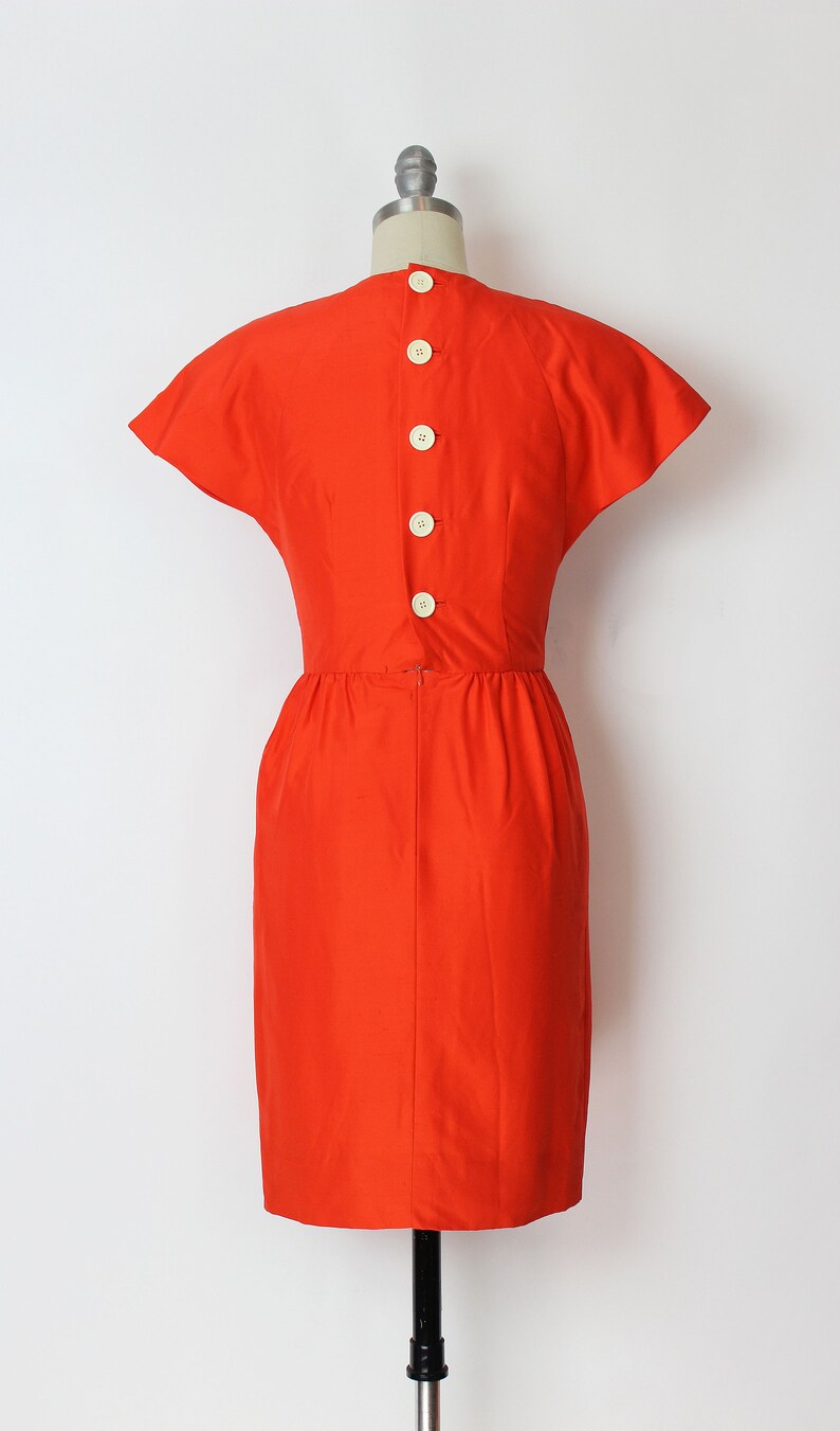 May include: A bright orange dress with short sleeves and a button-up back.