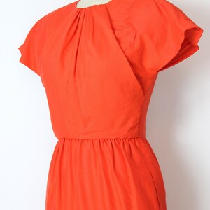 May include: A bright orange dress with a fitted bodice and a gathered skirt. The dress has short, cap sleeves and a round neckline.