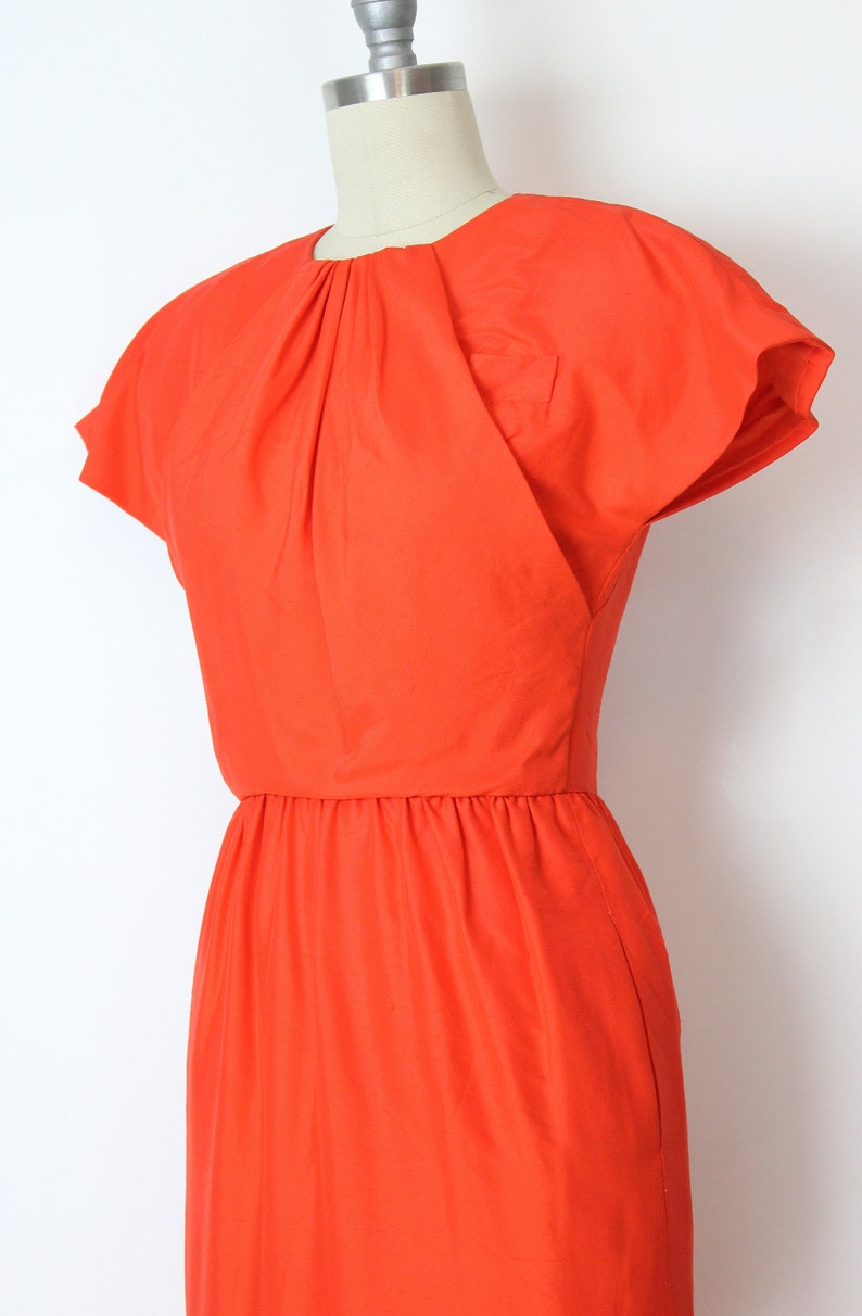 May include: A bright orange dress with a fitted bodice and a gathered skirt. The dress has short, cap sleeves and a round neckline.
