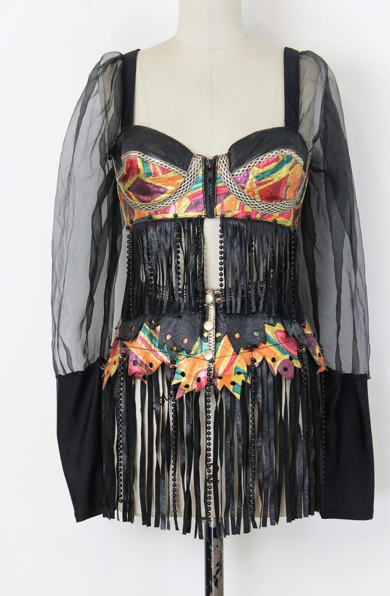 May include: A black and colorful bustier-style top with fringe and beaded accents. The top features a colorful, patterned design on the bodice and waist, with long black fringe and black sleeves.