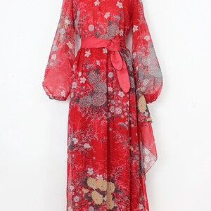 May include: A red maxi dress with a floral print and a matching red sash. The dress has long sleeves and a flowing skirt.