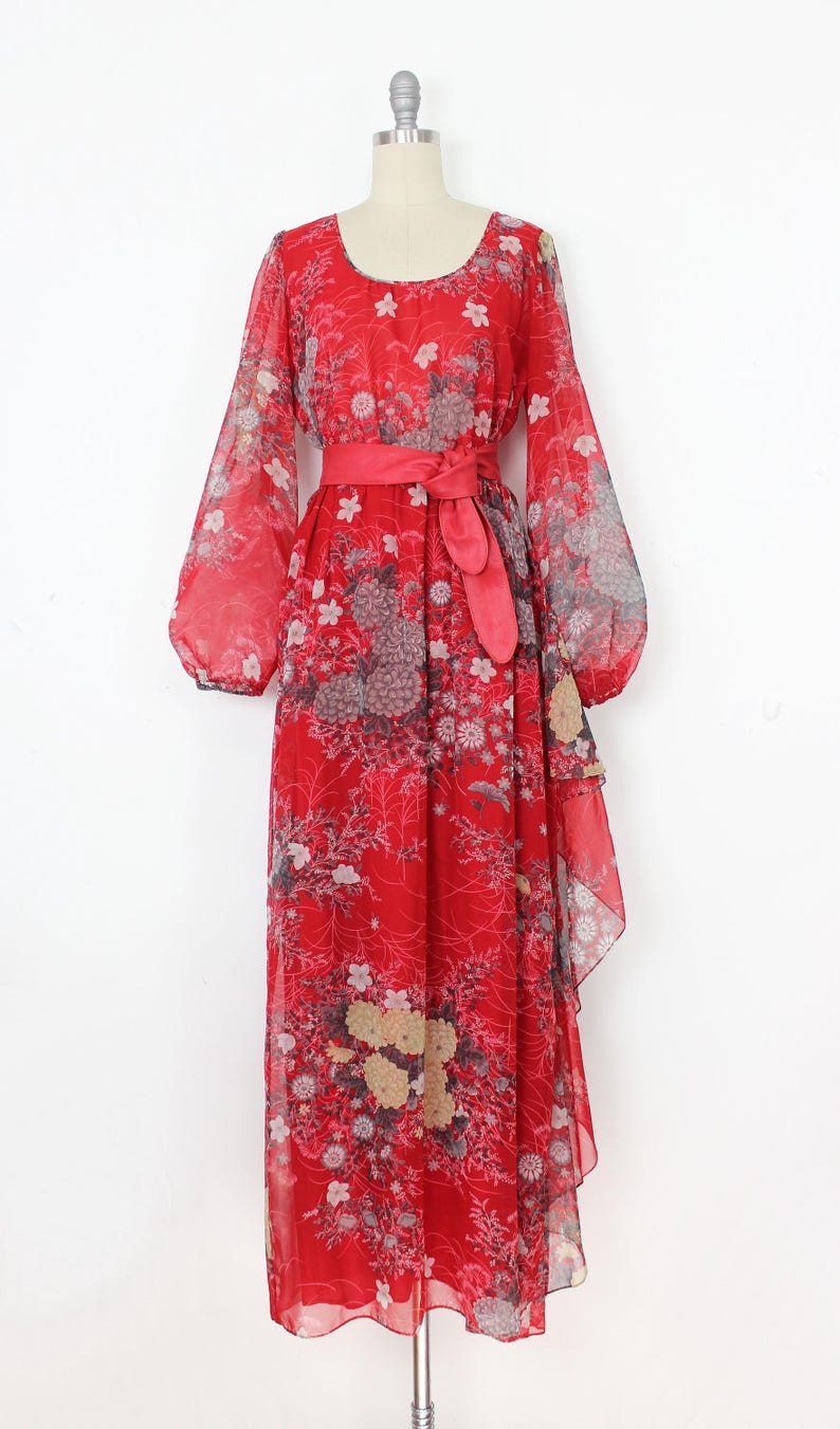 May include: A red maxi dress with a floral print and a matching red sash. The dress has long sleeves and a flowing skirt.