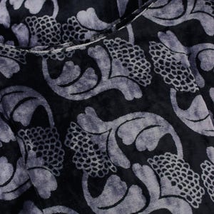 May include: Close-up of a dark fabric with a velvet texture. The fabric features a repeating pattern of stylized floral and leaf shapes in a lighter shade of gray, creating a contrast against the dark background. The design has a vintage or art nouveau feel.