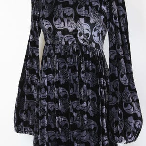 May include: A long black velvet dress with a gray floral pattern. The dress features long, voluminous sleeves and a gathered waist. The fabric has a soft, textured appearance, and the dress is displayed on a mannequin.