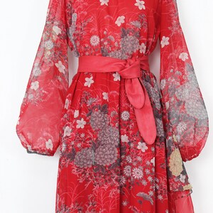 May include: A red maxi dress with a floral print and a matching red sash. The dress has long sleeves and a flowing skirt.