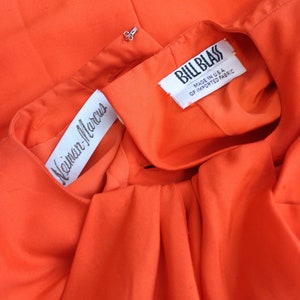 May include: Close-up of a bright orange fabric with two white labels. The top label reads "Bill Blass" and the bottom label reads "Neiman-Marcus".
