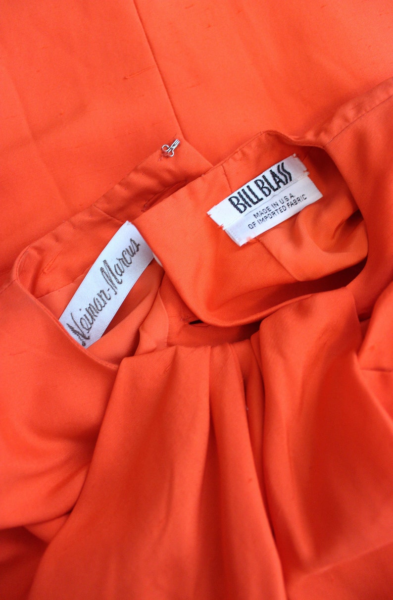 May include: Close-up of a bright orange fabric with two white labels. The top label reads "Bill Blass" and the bottom label reads "Neiman-Marcus".