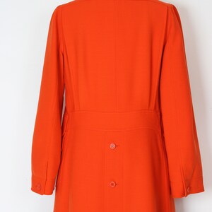 May include: A long, bright orange coat with a collar and a row of buttons down the back.
