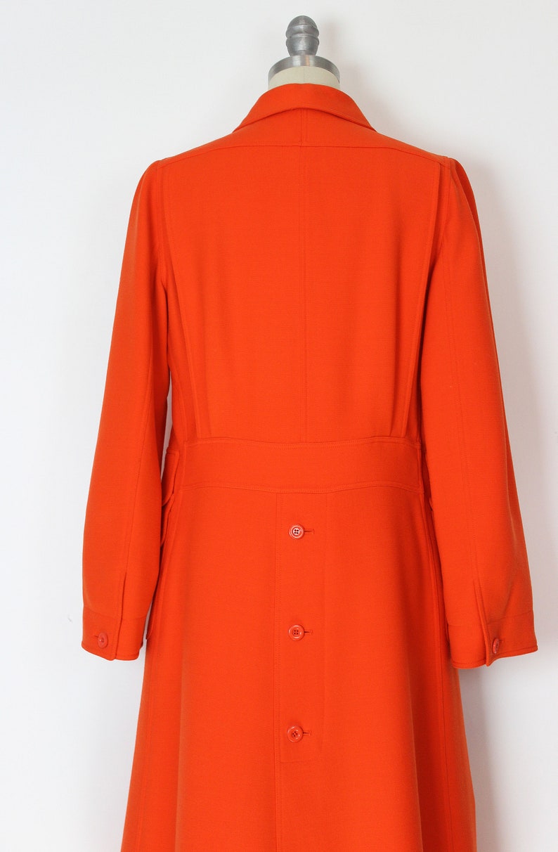 May include: A long, bright orange coat with a collar and a row of buttons down the back.