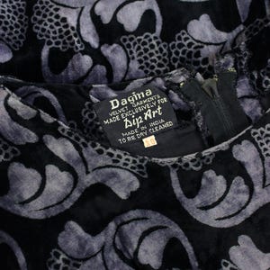 May include: Close-up of a black velvet garment with a repeating floral pattern in shades of gray. The garment has a zipper and a tag that reads "Dagina VELVET GARMENTS MADE EXCLUSIVELY FOR Dip Art MADE IN INDIA TO BE DRY CLEANED".