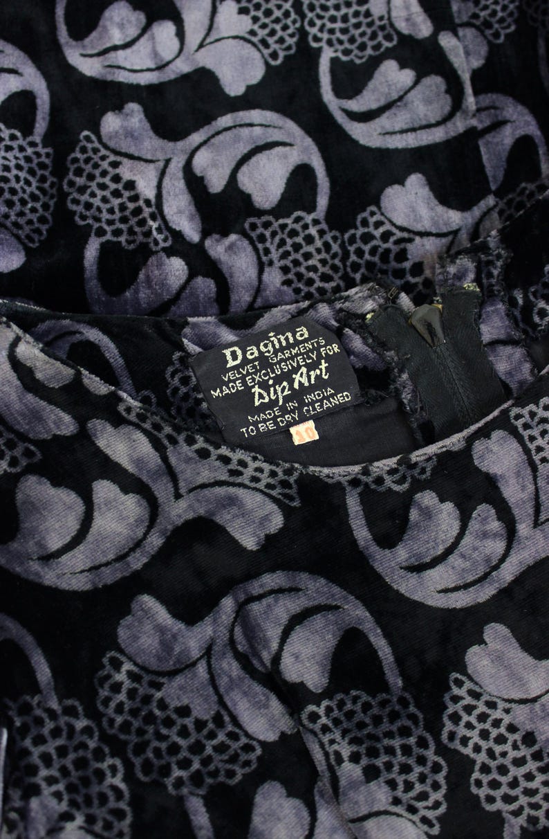 May include: Close-up of a black velvet garment with a repeating floral pattern in shades of gray. The garment has a zipper and a tag that reads "Dagina VELVET GARMENTS MADE EXCLUSIVELY FOR Dip Art MADE IN INDIA TO BE DRY CLEANED".