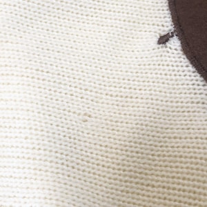 May include: Close-up of a white knitted fabric with a brown fabric patch in the upper right corner.