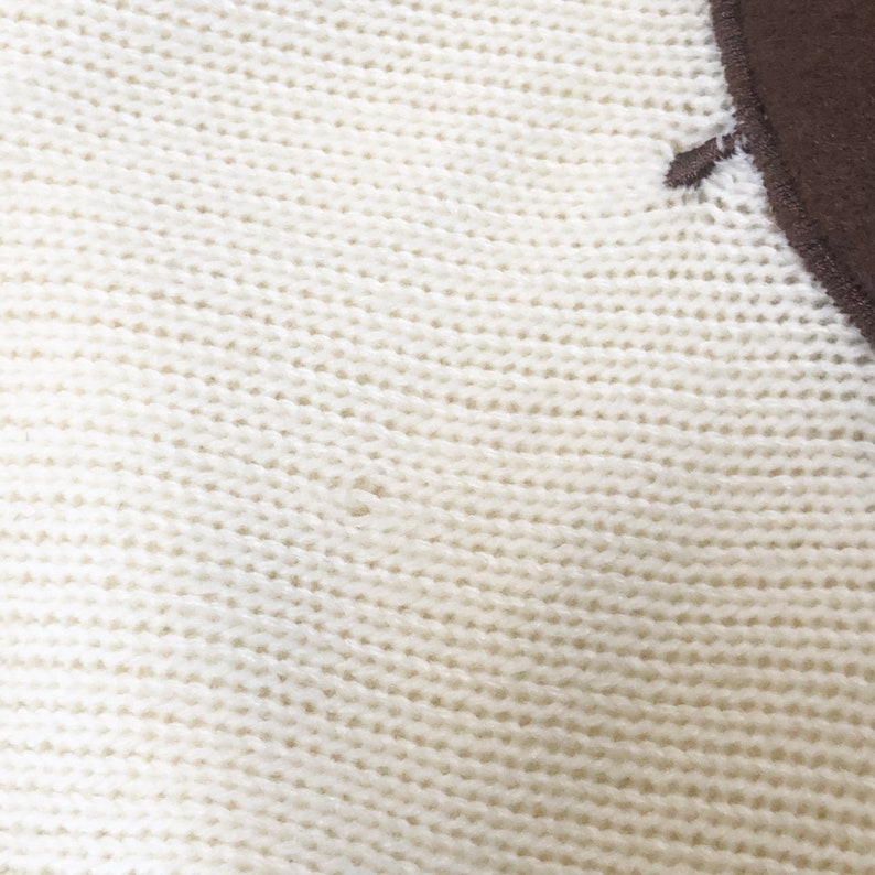 May include: Close-up of a white knitted fabric with a brown fabric patch in the upper right corner.